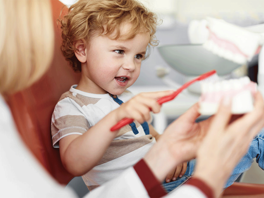 a young boy at the doctor practicing how to brush his teeth with the help of his doctor