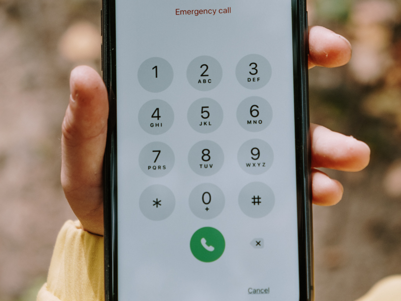 A photo of a person holding a cell phone. The screen of the phone says "emergency call."