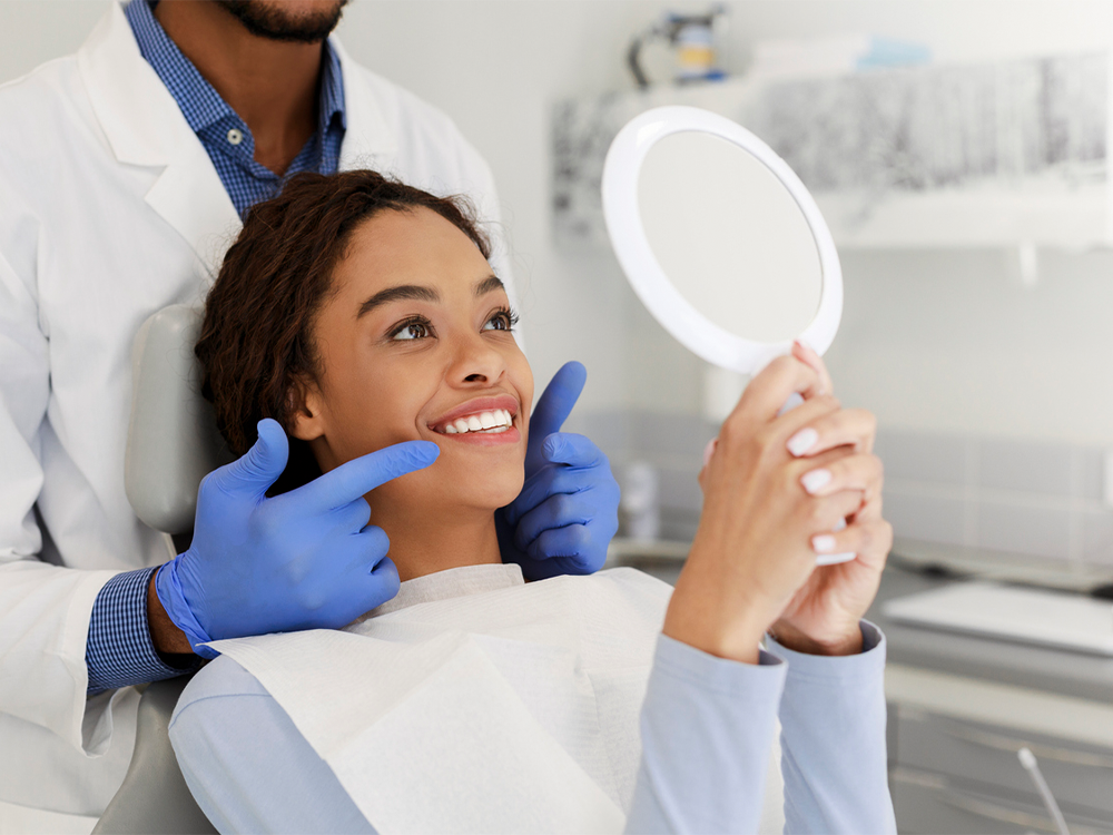 a young woman smiling at a mirror during a restorative dentistry appointment