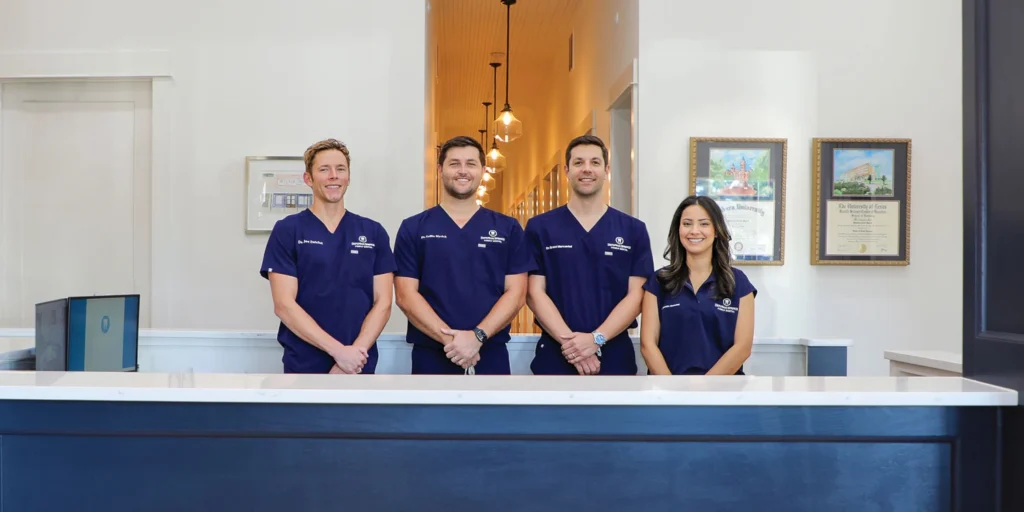 Dr. Collin Myrick, Dr. Grant Marcantel, Dr. Joe Zwickel, Dr. Esmeralda Marcantel standing behind the front desk of DeFuniak Springs Family Dental.